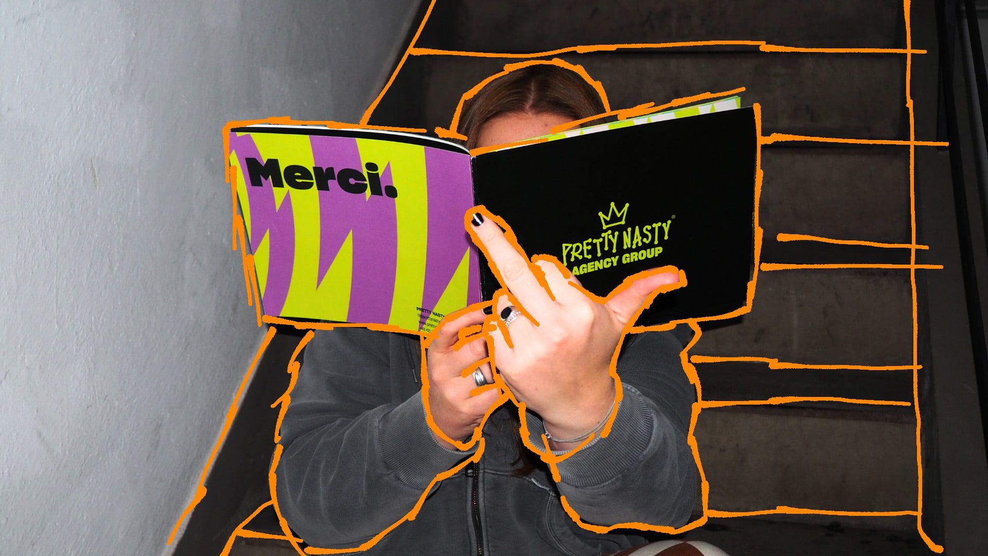 Startseite PRETTY NASTY Mitarbeiterin liest Brand Book und zeigt den Mittelfinger in die Kamera